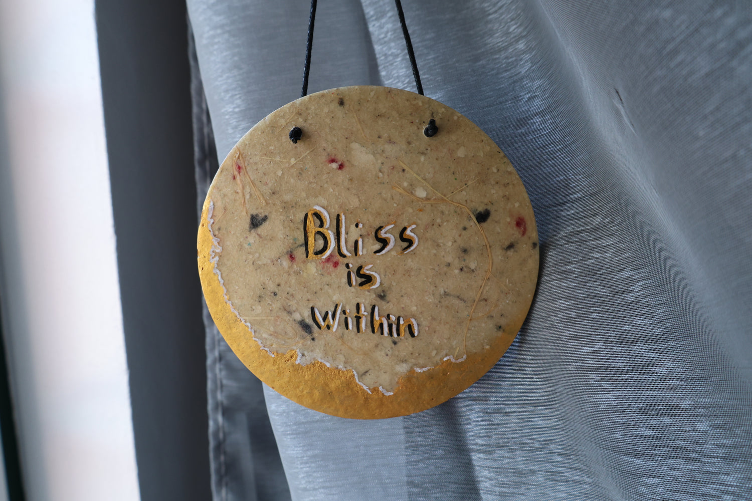 Round decorative item with 'Bliss is within' text on a plain surface